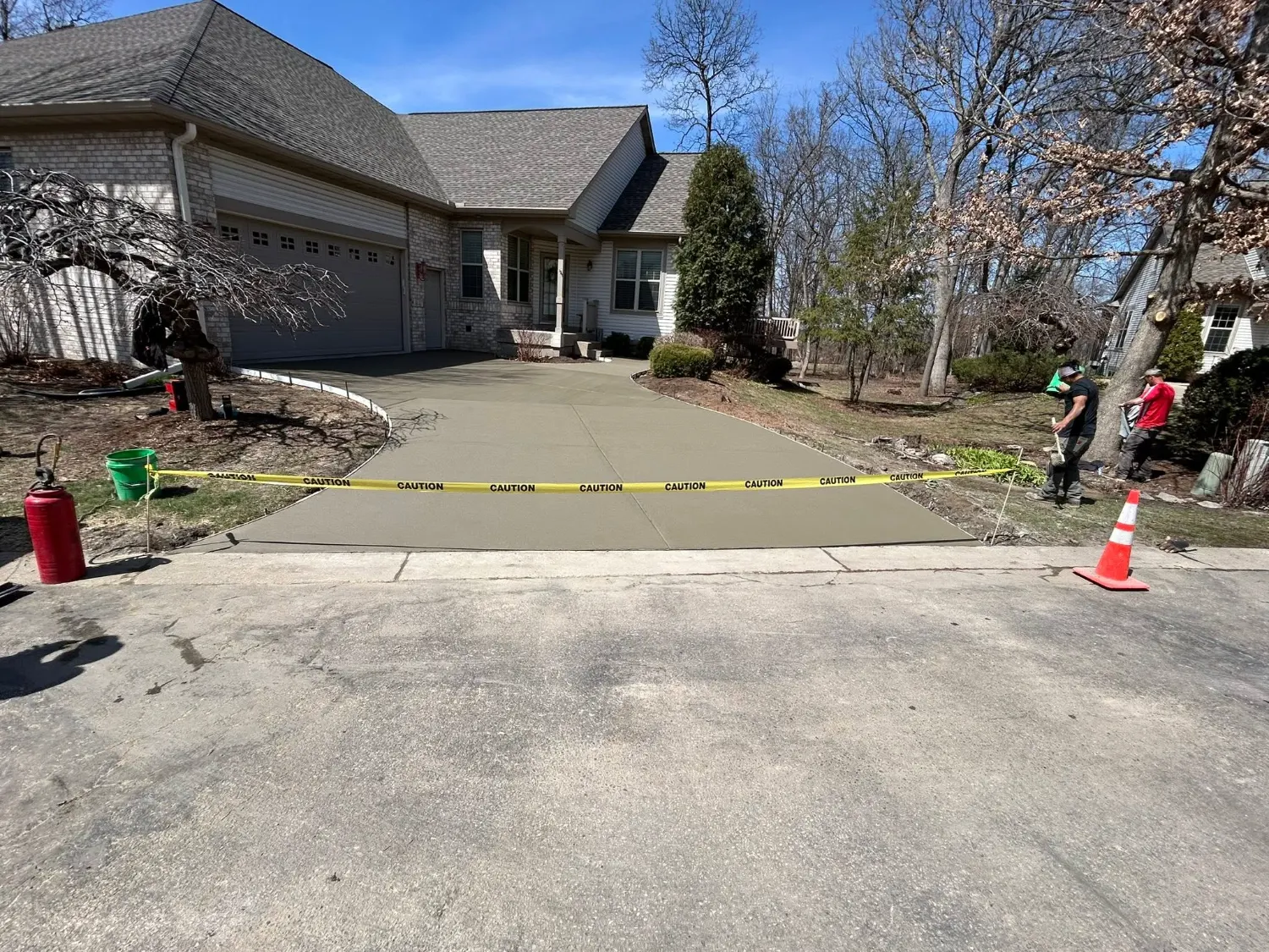 Freshly finished concrete driveway with caution tape and two crew members working at the edge